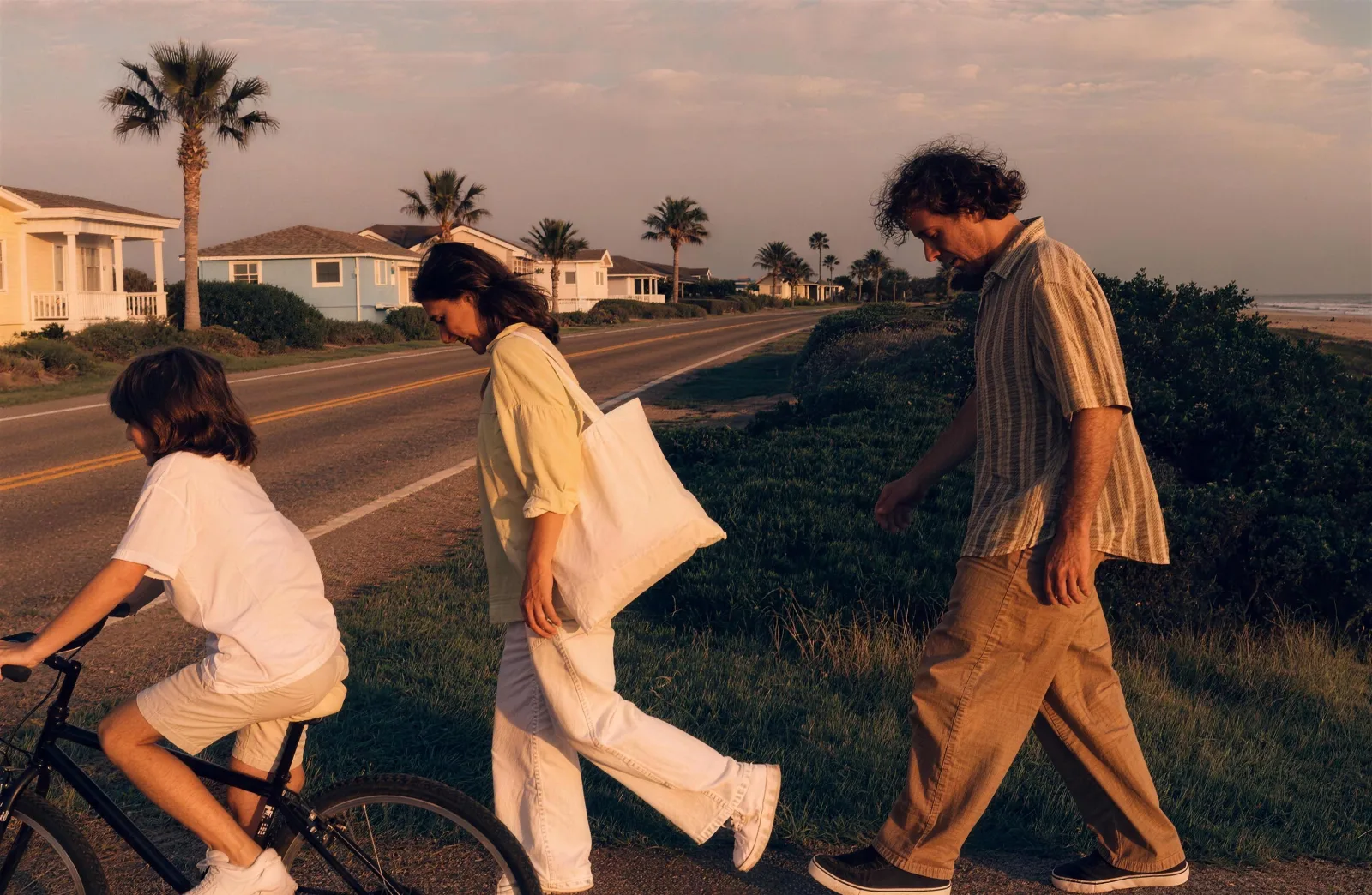 Family walking a paved coastal path at golden hour, one child ahead on a bike